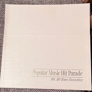 May include: A white book with the title "Popular Music Hit Parade" and the subtitle "110 All-Time Favorites" printed in gold lettering.