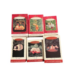 May include: Six Hallmark Keepsake Ornament boxes featuring cat-themed designs. The boxes display illustrations of kittens in various settings, including a suitcase, a birdcage, a cookie jar, and a basket, with text labels like Cat Naps and Mischievous Kittens.