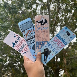 Op de afbeelding: Vier kleurrijke bladwijzers met hockeythema's. De bladwijzers bevatten tekst zoals "In My Hockey Romance", "You Had Me At Hockey", "Screw Prince Charming Give Me A Fictional Hockey Player", en "I Like My Books Spicy And My Men Icy".