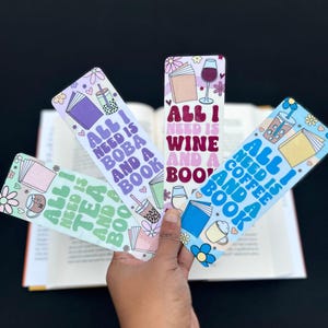 May include: Four colorful bookmarks with different designs and text. The bookmarks feature illustrations of books, drinks, and hearts. The text on the bookmarks reads "All I need is boba and a book", "All I need is wine and a book", "All I need is tea and a book", and "All I need is coffee and a book".