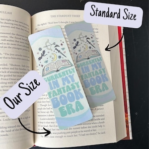 May include: Two blue and green bookmarks with the text "Currently in my fantasy book era" in a whimsical font. The bookmarks feature a book, a crescent moon, stars, a dagger, an arrow, and bats.