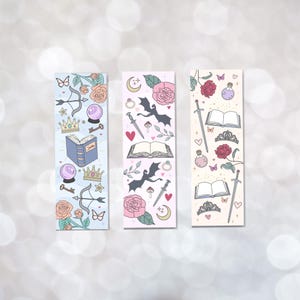 May include: Three colorful bookmarks with a fantasy theme. Each bookmark features a different design with illustrations of a dragon, a crown, a book, a sword, a heart, a butterfly, a key, a potion bottle, a moon, a rose, and other magical elements.