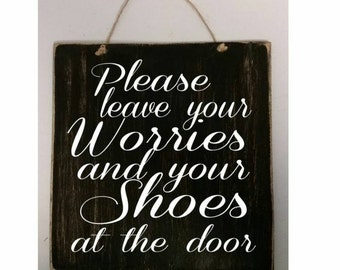 May include: A black wooden sign with white text that reads "Please leave your worries and your shoes at the door".