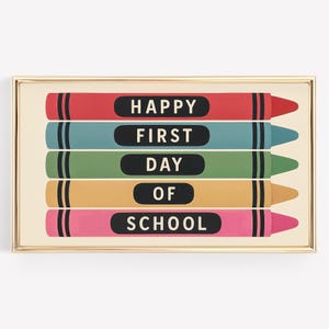 May include: A framed print featuring five colorful crayon illustrations. Each crayon is a different color: red, blue, green, yellow, and pink. The text "HAPPY FIRST DAY OF SCHOOL" is printed on the crayons in black.