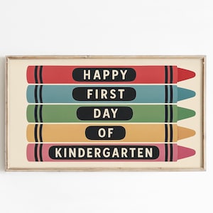 May include: A framed print featuring five colorful crayon illustrations. Each crayon is a different color: red, teal, green, yellow, and pink. The words "HAPPY FIRST DAY OF KINDERGARTEN" are printed on the crayons in white text on black ovals.