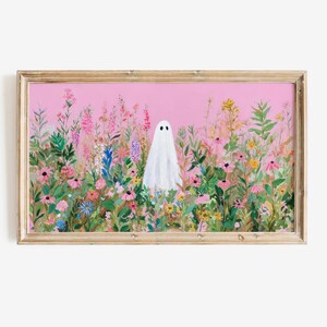 May include: A framed art print featuring a white ghost figure standing in a field of colorful wildflowers. The artwork has a pink background and is set in a light brown wooden frame. The flowers are in shades of pink, purple, yellow, and green.