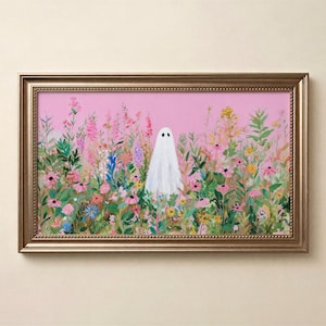 May include: A framed art print featuring a whimsical ghost in a field of colorful wildflowers. The artwork has a pink background and is enclosed in a gold-colored frame. The ghost is white with two black dot eyes.
