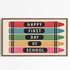 May include: A framed print featuring five colorful crayons in red, teal, green, yellow, and pink. Each crayon has a black label with white text that reads "HAPPY FIRST DAY OF SCHOOL". The artwork is set against a cream background.