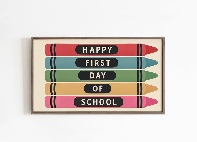 May include: A framed print featuring five colorful crayons in red, teal, green, yellow, and pink. Each crayon has a black label with white text that reads "HAPPY FIRST DAY OF SCHOOL". The artwork is set against a cream background.