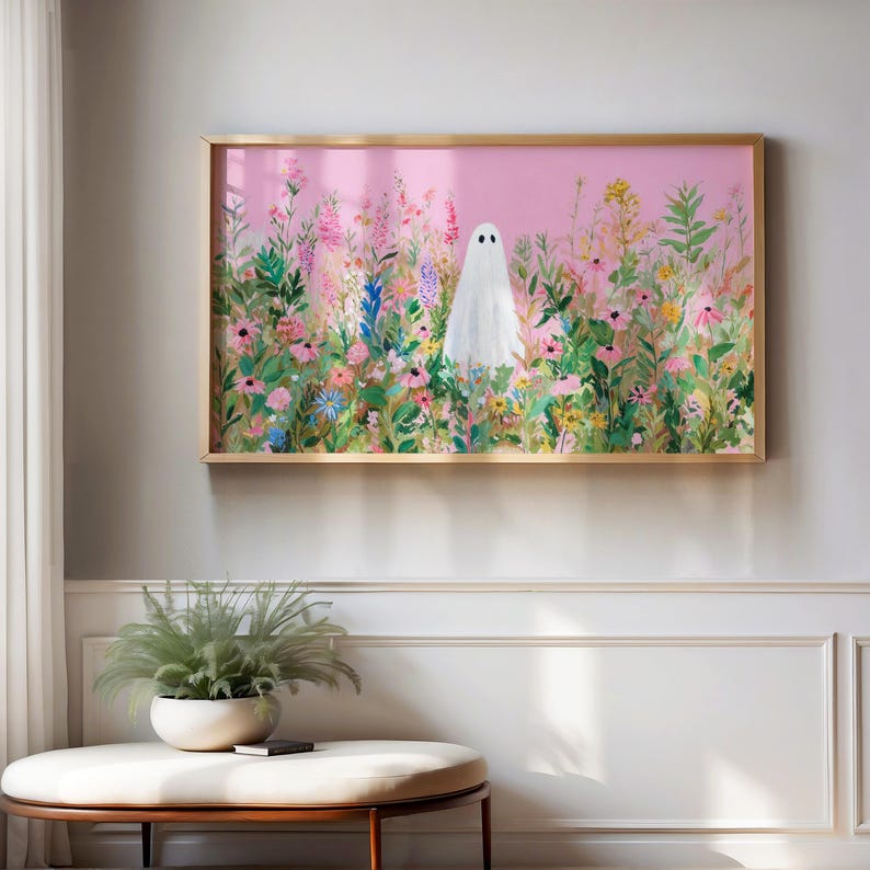 May include: A framed art print featuring a white ghost figure standing in a field of colorful wildflowers against a pink background. The artwork is enclosed in a gold-colored frame, adding a touch of elegance to the whimsical scene.