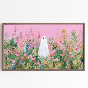 May include: A framed art print featuring a white ghost figure standing in a field of colorful wildflowers. The background is a soft pink, and the frame is a muted brown. The artwork has a whimsical, nature-inspired theme.
