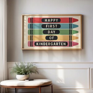 May include: A framed print featuring five colorful crayon illustrations. Each crayon is a different color: red, blue, green, yellow, and pink. The text "HAPPY FIRST DAY OF KINDERGARTEN" is displayed on the crayons in black.