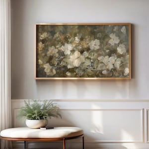 Op de afbeelding: Een ingelijst bloemenschilderij met witte bloesems en groene bladeren tegen een gedempte achtergrond. Het kunstwerk zit in een goudkleurige lijst. Het schilderij wordt op een lichtgrijze muur getoond.