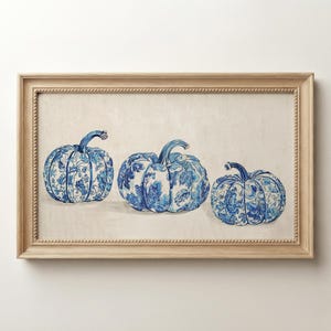Könnte beinhalten: Ein rechteckiges gerahmtes Wandbild mit einer horizontalen Illustration von drei Kürbissen. Jeder Kürbis ist mit einem blau-weißen Blumenmuster auf hellcremefarbenem Hintergrund verziert und befindet sich in einem hellen Holzrahmen mit Perlenleiste.