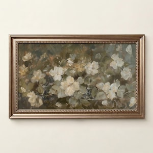 Op de afbeelding: Een ingelijst bloemenschilderij met witte en gele bloemen met groene bladeren. Het kunstwerk is geplaatst tegen een gedempte achtergrond en omlijst in een goudkleurige, sierlijke lijst. Het schilderij roept een gevoel van natuur en rust op.