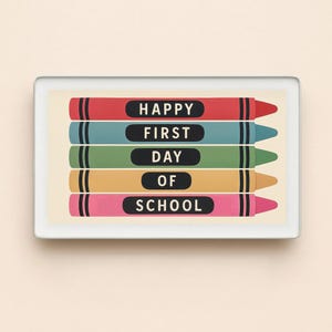May include: A rectangular print featuring five horizontal crayons in red, blue, green, yellow, and pink. Each crayon contains a black label with white text reading HAPPY, FIRST, DAY, OF, SCHOOL, stacked vertically within a thin white frame.