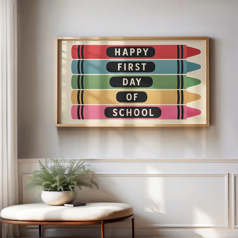 May include: A framed print featuring colorful crayon illustrations. Each crayon displays the words "HAPPY FIRST DAY OF SCHOOL" in black text. The crayons are red, blue, green, yellow, and pink. The frame is gold.