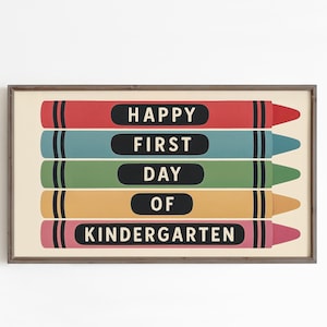 May include: A framed print featuring colorful crayon illustrations. Each crayon is a different color: red, teal, green, yellow, and pink. The words "HAPPY FIRST DAY OF KINDERGARTEN" are printed on the crayons in white text.