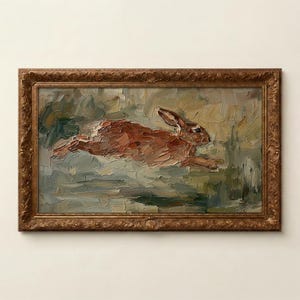 May include: Oil painting of a running rabbit in a decorative gold frame. The rabbit is rendered in shades of brown and tan, set against a backdrop of green and gray brushstrokes. The frame has an ornate, textured design.