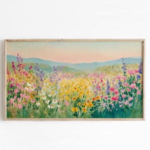 May include: A rectangular landscape painting in a light wood frame depicting a vibrant wildflower meadow with yellow, pink, and purple blooms under a soft pastel sky. The scene features rolling hills in the distance and lush green foliage.