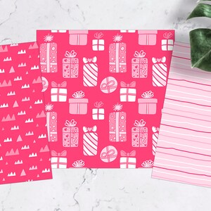 May include: Three pink patterned sheets of wrapping paper. The first sheet has a pattern of white triangles, the second sheet has a pattern of white gift boxes, and the third sheet has a pattern of white stripes.
