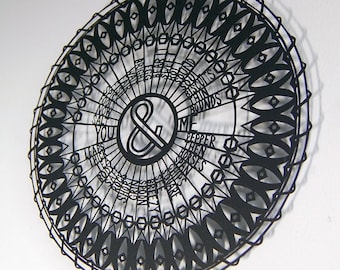 May include: A black and white paper cut design of a circle with a decorative border and the words "& Me" in the centre. The words "You", "Salt", "Leaves", "Thick", "Spice", "Fool's", "Bright", "Grin", "Short", "Biscuits", "Bound", "Pepper", "Horses", "Scents", "Ground", "Fish", "Be", "M" are arranged in a circle around the centre.