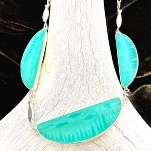 May include: A turquoise and silver necklace with a unique design. The necklace features three large, half-moon shaped turquoise pendants with a textured surface, connected by silver chain links. The turquoise pendants are outlined in silver.