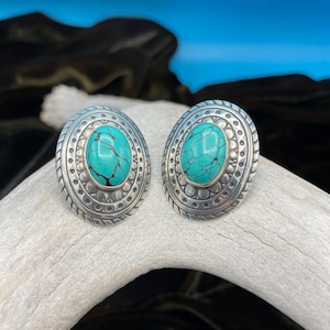 May include: A pair of silver earrings with turquoise stones set in a circular design.