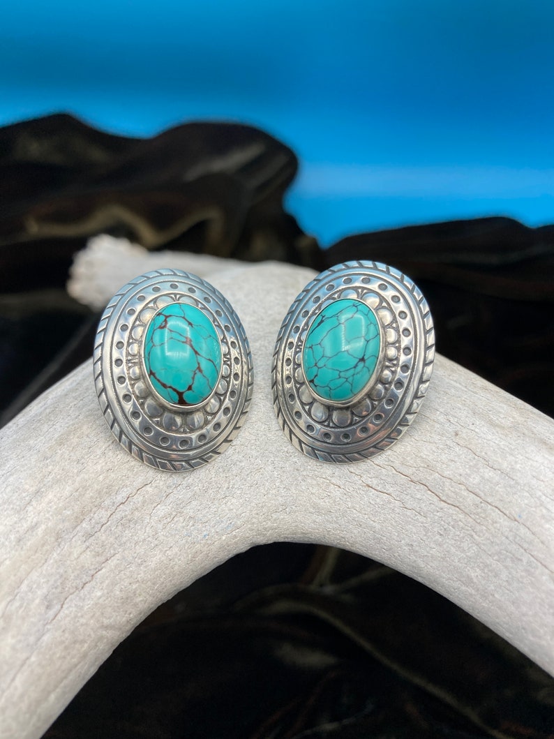 May include: A pair of silver earrings with turquoise stones set in a circular design.