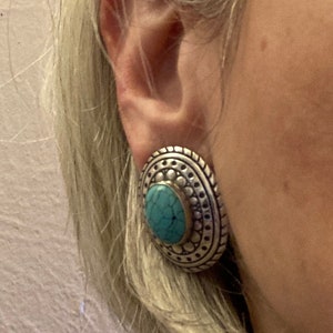 May include: Silver and turquoise statement earrings with a circular design. The earrings have a textured surface and a turquoise stone in the centre.