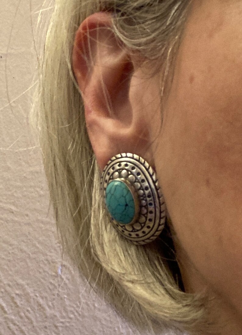 May include: Silver and turquoise statement earrings with a circular design. The earrings have a textured surface and a turquoise stone in the centre.
