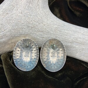 May include: A pair of silver earrings with a detailed design. The back of the earrings are stamped with "TK Sterling".