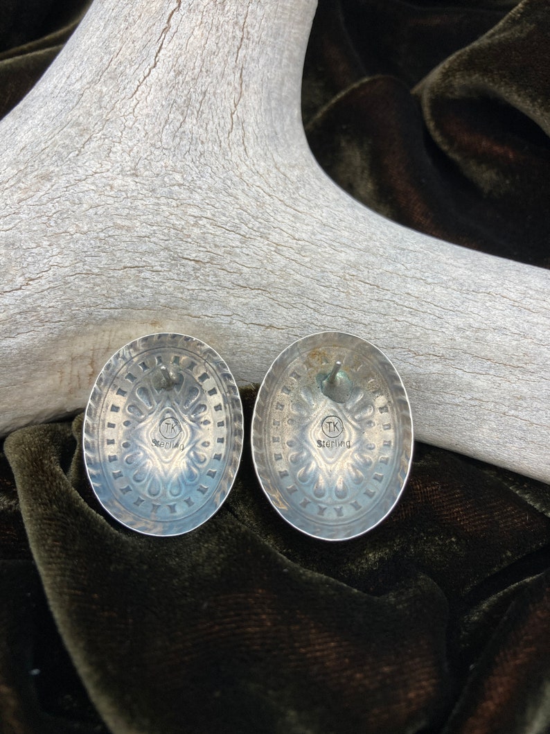 May include: A pair of silver earrings with a detailed design. The back of the earrings are stamped with "TK Sterling".