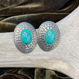 May include: A pair of silver earrings with turquoise stones set in a circular design.