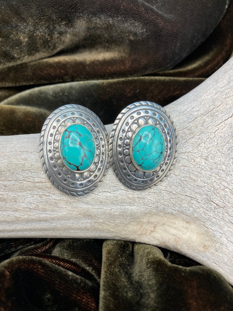May include: A pair of silver earrings with turquoise stones set in a circular design.