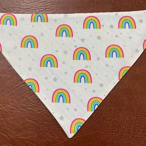 May include: White triangular bandana with a repeating pattern of colorful rainbows and silver glitter stars.