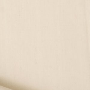 May include: A close-up of a plain, off-white fabric with a subtle texture. The fabric is folded over on itself, creating a soft, curved edge.