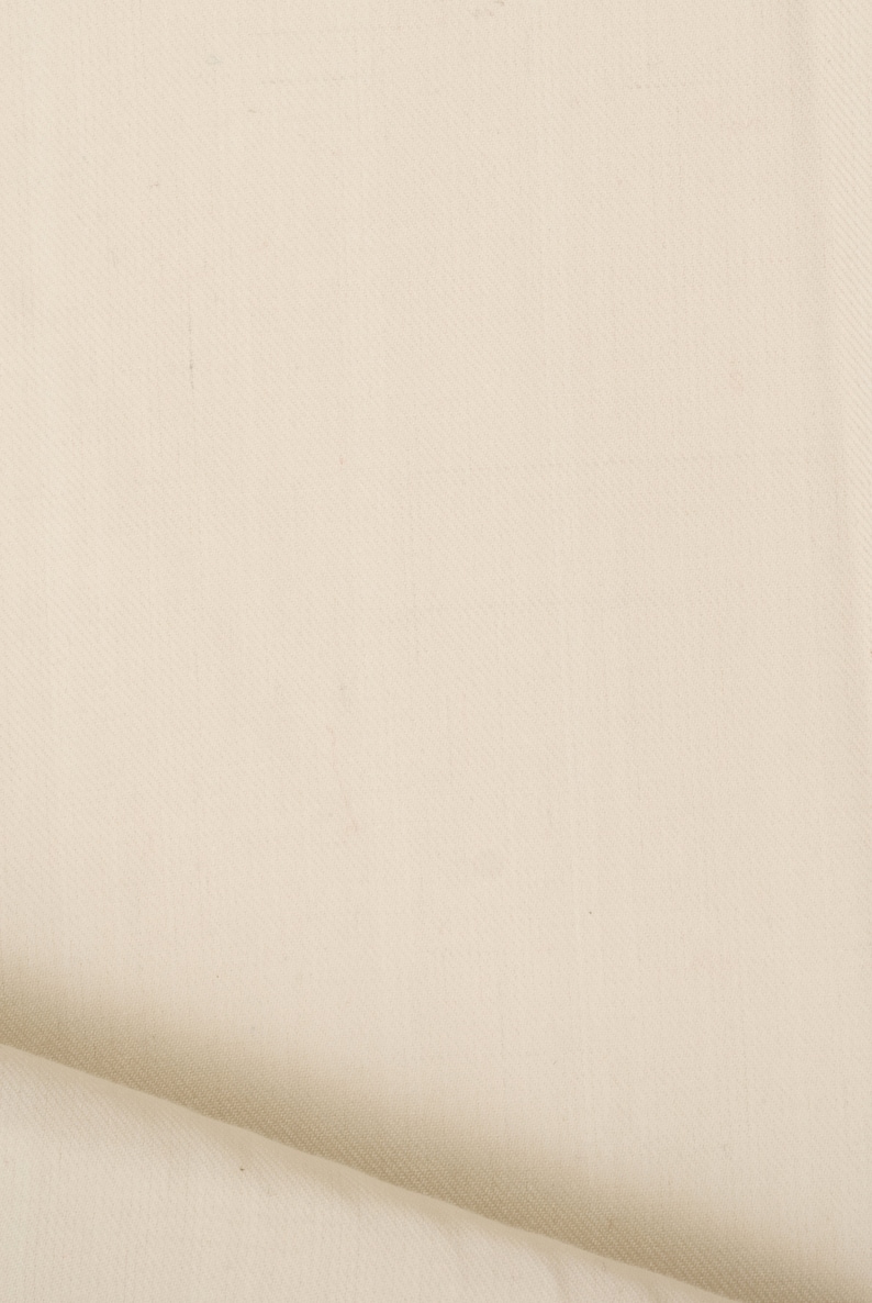 May include: A close-up of a plain, off-white fabric with a subtle texture. The fabric is folded over on itself, creating a soft, curved edge.