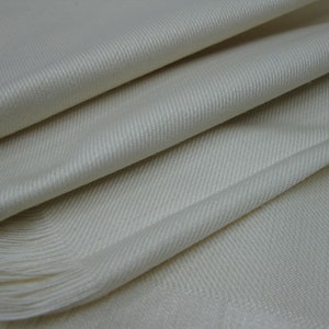 May include: A white woven scarf with a fringe edge. The scarf is made of a soft, luxurious fabric.
