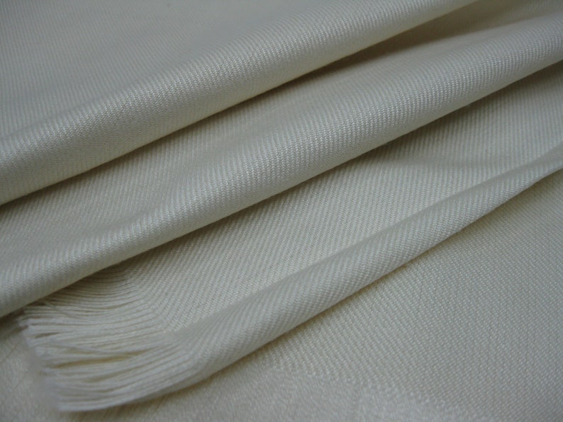 May include: A white woven scarf with a fringe edge. The scarf is made of a soft, luxurious fabric.