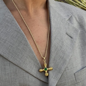 May include: A gold chain necklace with a green gemstone cross pendant. The cross has a detailed design with four arms and a round center stone.