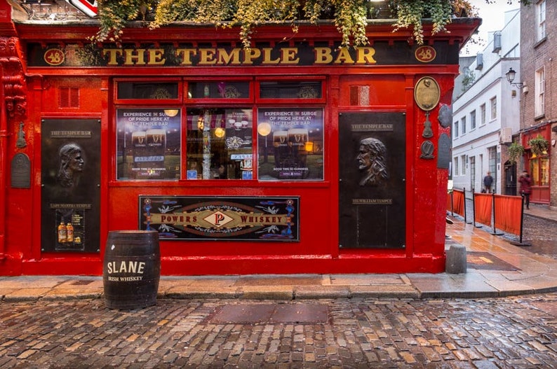 Puede incluir: El pub Temple Bar en Dubl&iacute;n, Irlanda, con una fachada roja, letras doradas y un letrero que dice "The Temple Bar". Hay un barril de whisky irland&eacute;s Slane frente al pub.