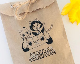 May include: A brown paper bag with a black and white illustration of a girl and a cat in a car. The text "Alanna's Dollhouse" is printed on the bag.