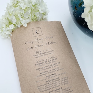 Peut inclure: Un programme de mariage en papier brun avec du texte noir. Le programme &eacute;num&egrave;re les noms des mari&eacute;s, la date, le lieu et le cort&egrave;ge nuptial. Des fleurs blanches sont en arri&egrave;re-plan.