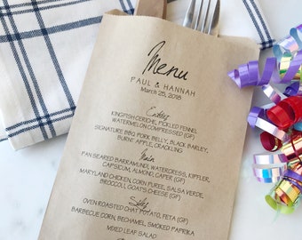 May include: A kraft paper menu with the names "Paul & Hannah" and the date "March 25, 2018" printed in black. A fork and a wooden knife are in the menu pocket. A blue and white checkered napkin and colorful party streamers are in the background.