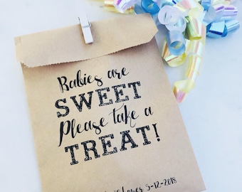 May include: A brown paper treat bag with the text "Babies are SWEET Please take a TREAT!" and "Lan's Baby Shower 5-12-2018". The bag is clipped shut with a white clip and decorated with iridescent ribbon.