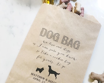 May include: A brown paper dog bag filled with dog treats. The bag has the words "DOG BAG" printed at the top, along with a message and the names "MATTHEW & KELLEE" and the date "APRIL 22, 2018". Two dog silhouettes are also printed on the bag.