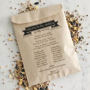 May include: A light brown paper packet filled with birdseed, featuring black printed text that reads Welcome to the wedding of Kelly and Greg, June 27, 2015, Estes Park, CO, along with a list of the wedding party members and parents.