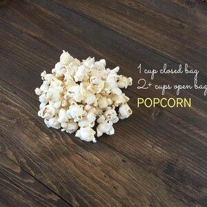 May include: A pile of freshly popped popcorn on a dark wooden surface. The image includes text indicating the yield: 1 cup for a closed bag and 2+ cups for an open bag. The word "POPOCRN" is also visible.