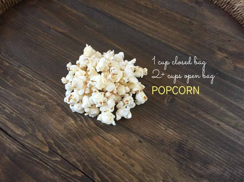 May include: A pile of freshly popped popcorn on a dark wooden surface. The image includes text indicating the yield: 1 cup for a closed bag and 2+ cups for an open bag. The word "POPOCRN" is also visible.